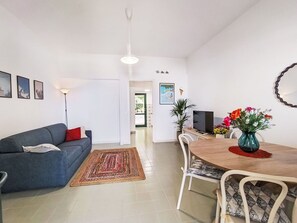 Ein modernes Wohnzimmer mit einer Couch, einem Esstisch mit Stühlen, einem Fernseher und einem Teppich.