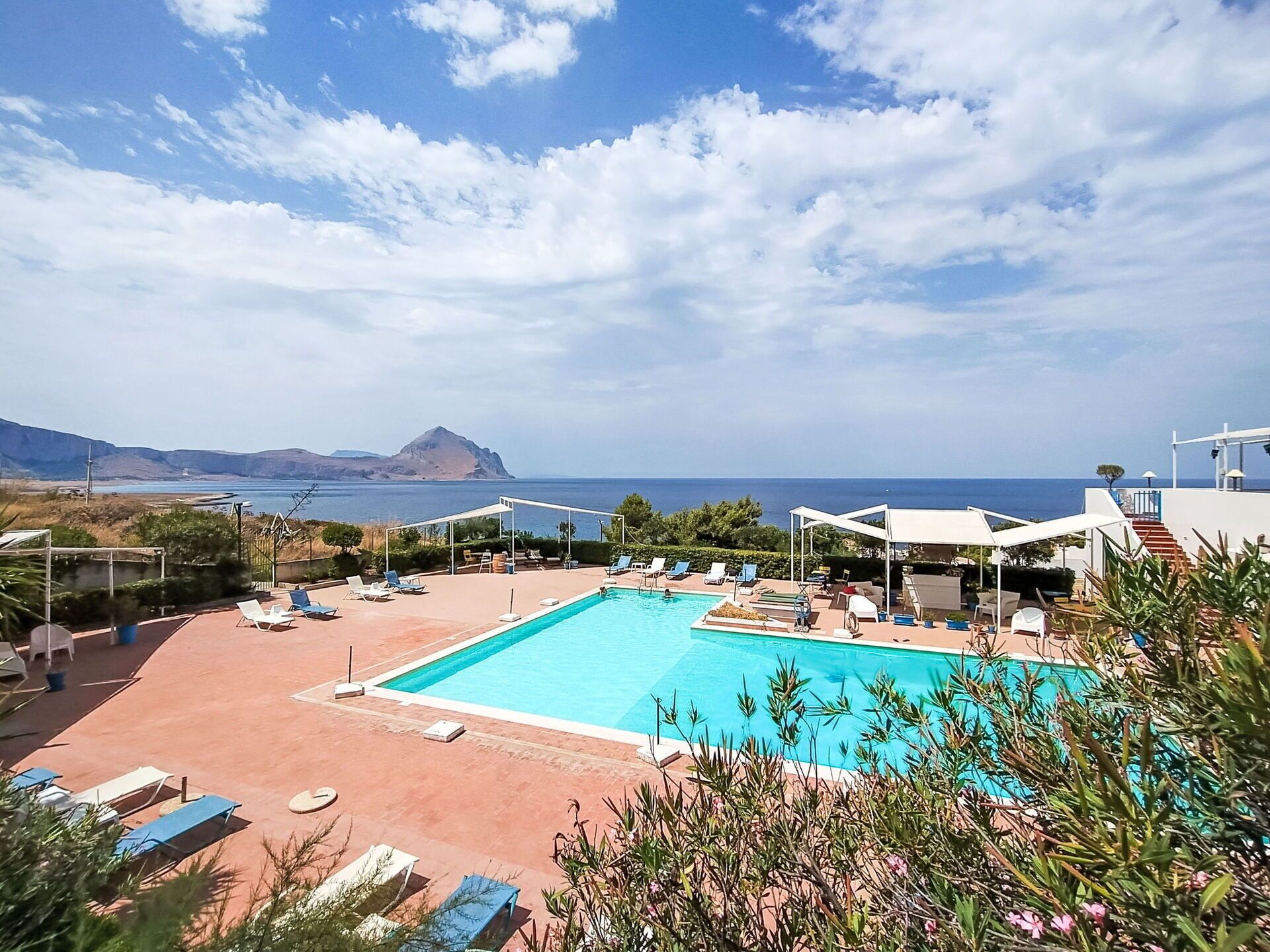 A swimming pool with lounge chairs and umbrellas, overlooking a body of water and a distant mountain.