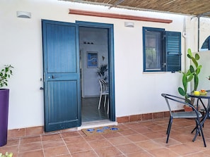 Ein Terrassenbereich mit einer Tür, einem Fenster mit Rollläden, einer Kakteenpflanze und einem Tisch mit Stühlen.