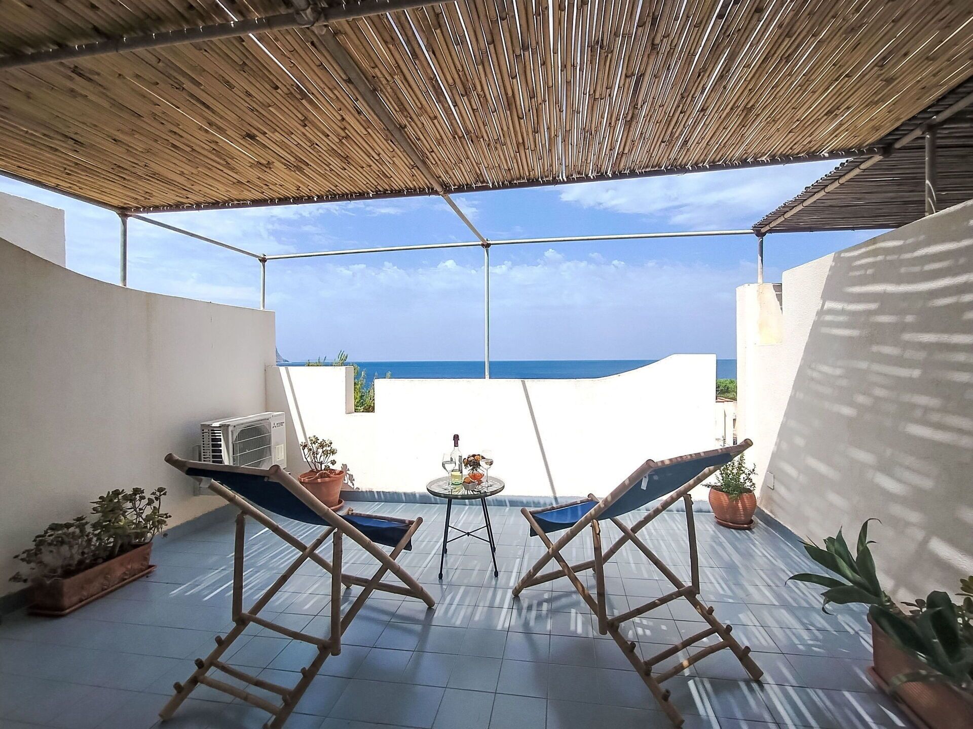 Un espace extérieur abrité comprenant deux chaises longues, une petite table avec une bouteille et des verres, et des plantes en pot.