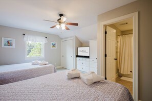 A bedroom with two beds, a ceiling fan, a window with curtains, a door, and a dresser. - Chandler Cottage, Charming Golf Cottage in Hampton Hall (Bluffton)