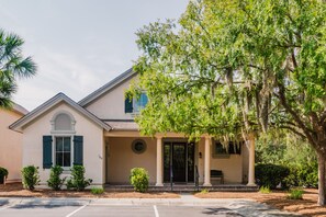 A two-story house with a front porch, a small front yard, and a tree. - Chandler Cottage, Charming Golf Cottage in Hampton Hall (Bluffton)