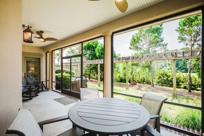 A covered patio with a round table and chairs, large windows, and a pergola. - Chandler Cottage, Charming Golf Cottage in Hampton Hall (Bluffton)