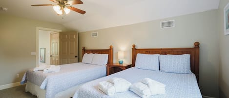 A hotel room with two beds, a ceiling fan, and a door leading to another room.