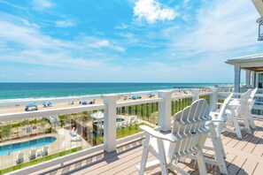 Ein Balkon mit weißen Stühlen mit Blick auf einen Strand und einen Poolbereich.