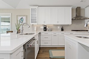 A modern kitchen with white cabinetry, stainless steel appliances, and a large island with a sink. - Oceanfront Luxury 8BR w/ Pool, Hot Tub, Theater, Game Room & Elevator (Atlantic Beach)