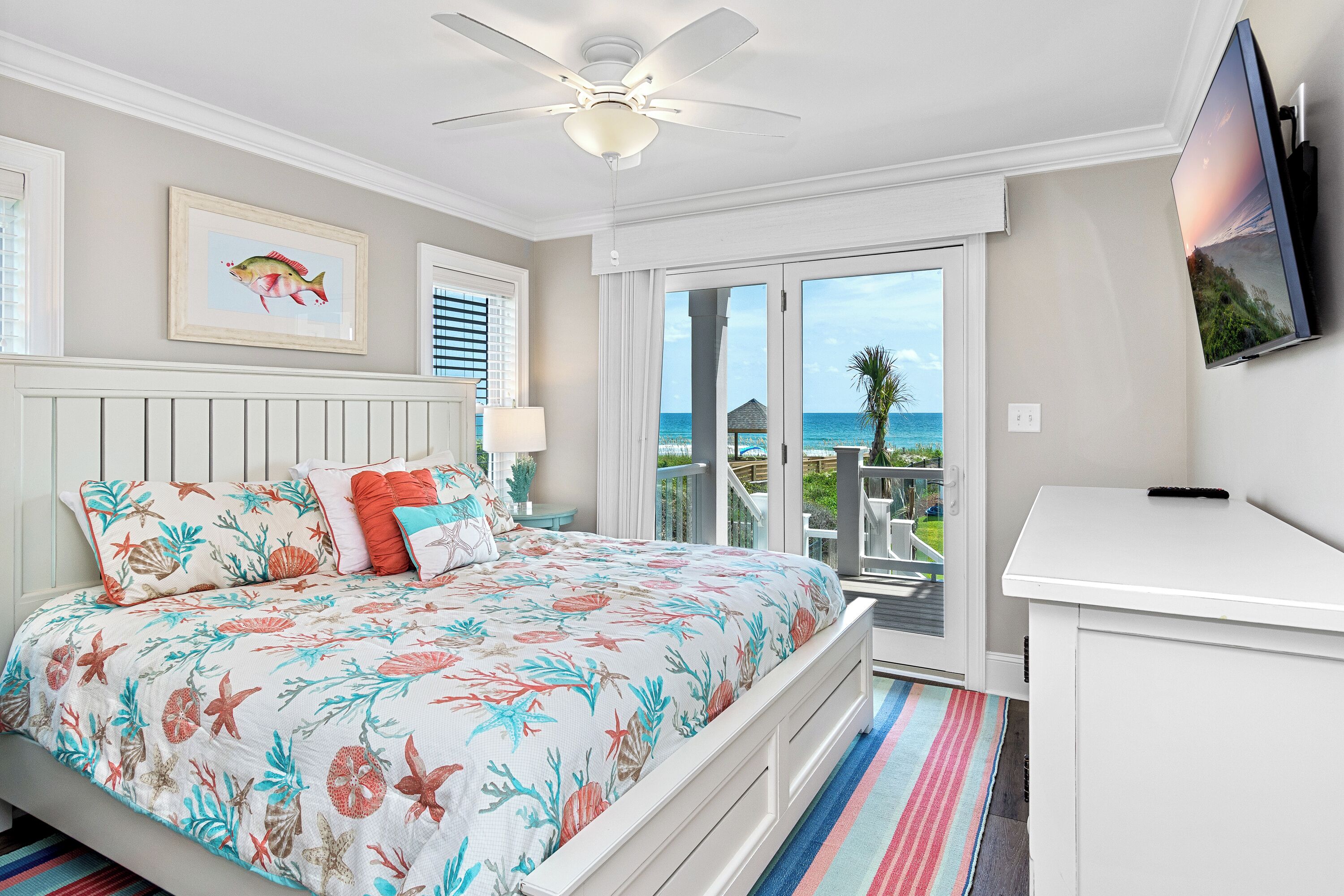 A bedroom with a bed, a ceiling fan, a TV, and a view of the ocean.