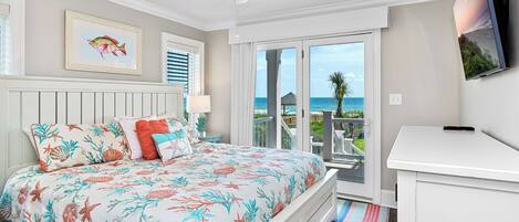 A bedroom with a bed, a ceiling fan, a TV, and a view of the ocean.
