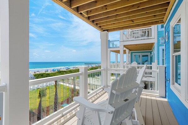 Un balcon avec vue sur la plage et l’océan, des meubles d’extérieur blancs et un plafond en bois.