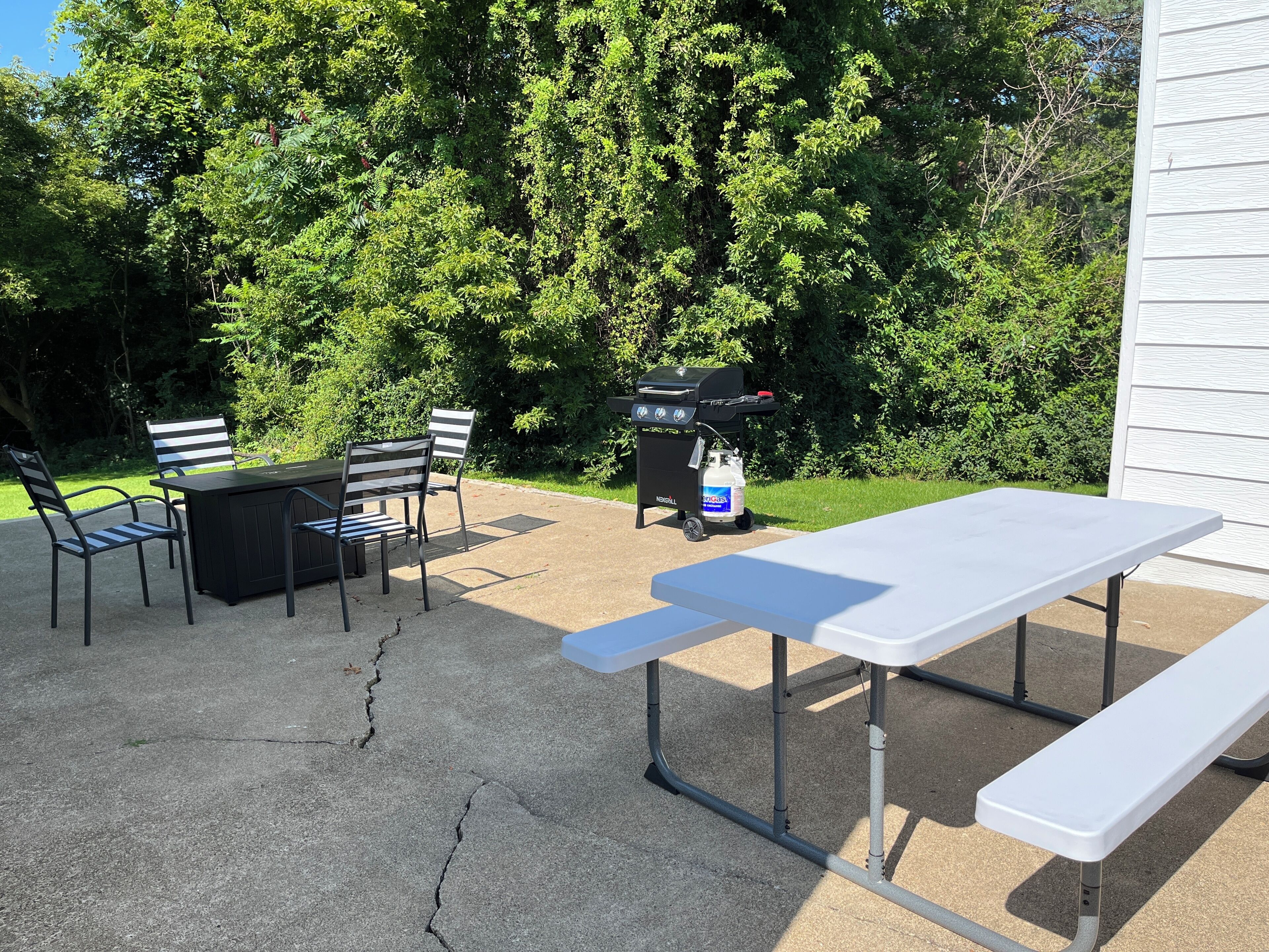Une terrasse extérieure avec une table et des chaises, un barbecue et une bouteille de gaz.