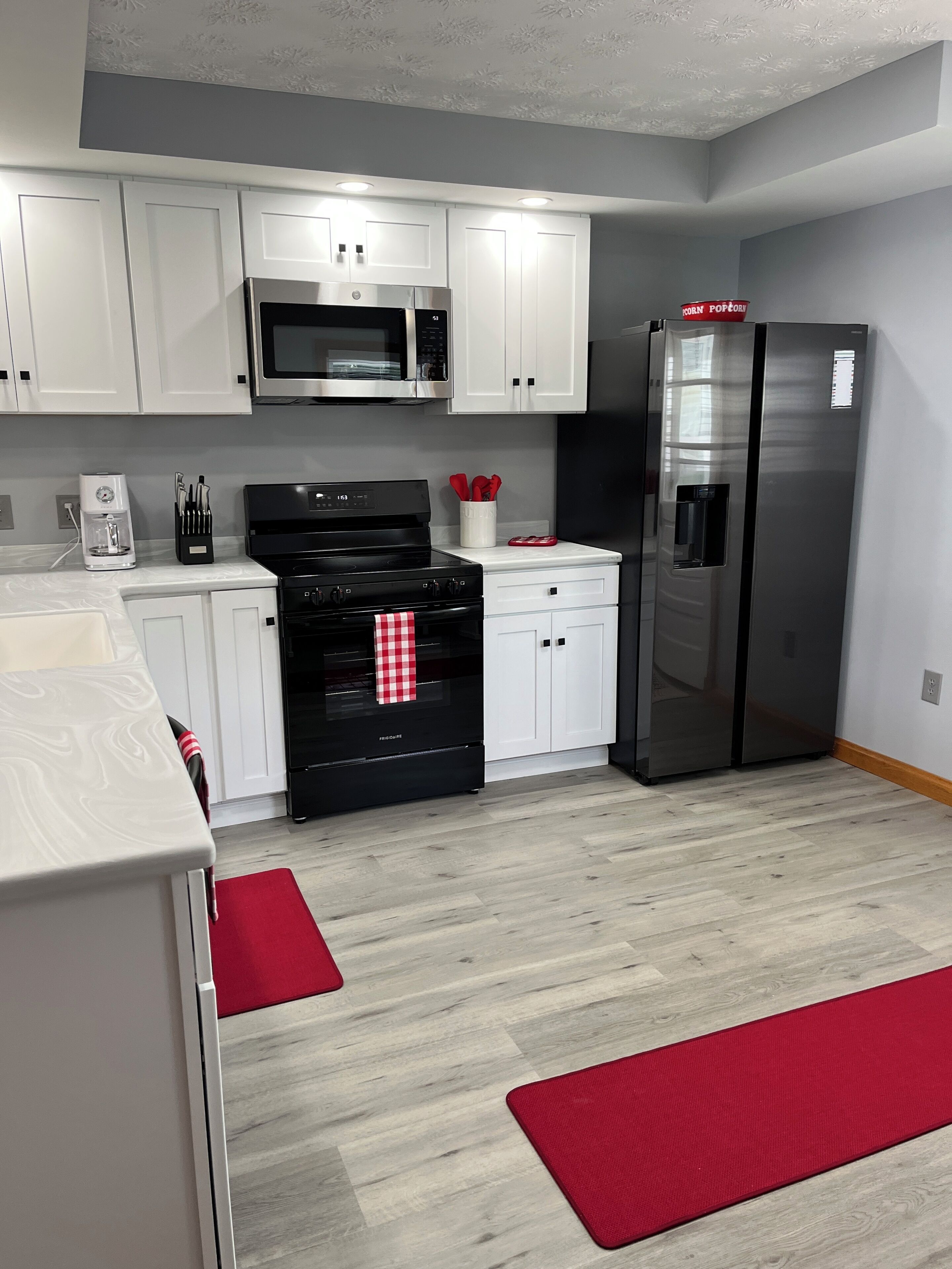 Une cuisine moderne avec des meubles blancs, une cuisinière noire, des appareils électroménagers en acier inoxydable et un tapis rouge.