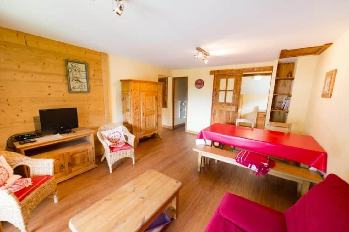Una sala de estar acogedora con televisor, muebles de madera y una mesa roja.
