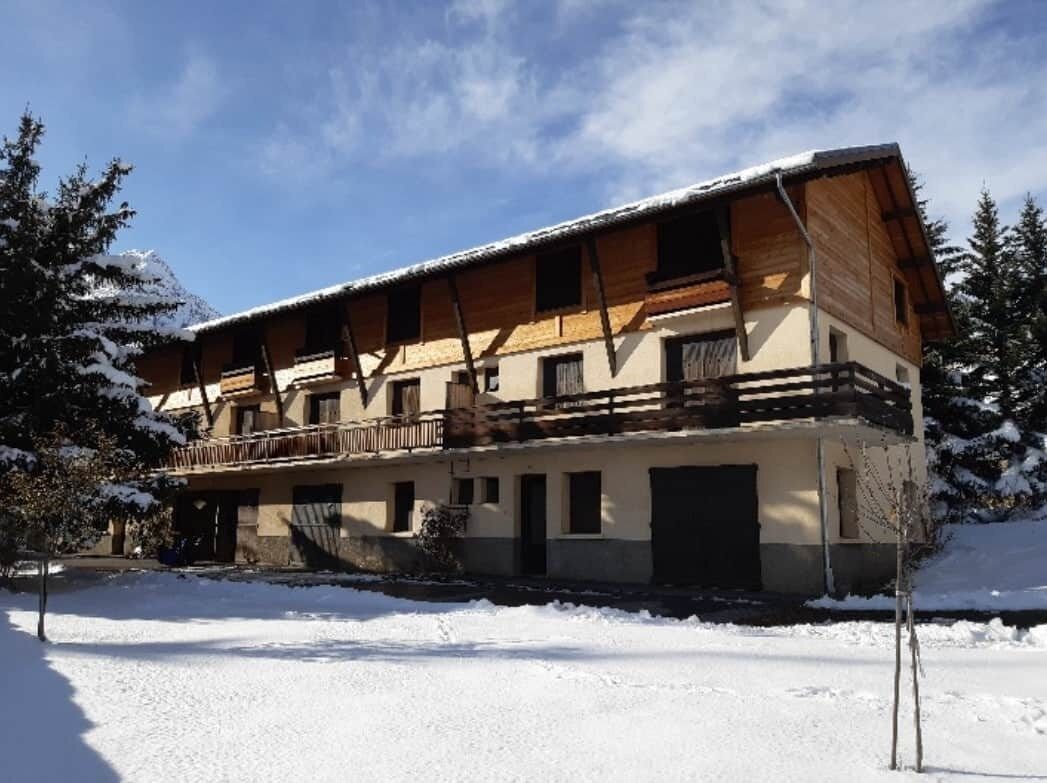 Un edificio de dos pisos con un balcón en el nivel superior, rodeado de árboles cubiertos de nieve.