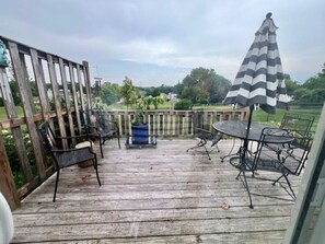 Una terraza de madera con mobiliario exterior, incluyendo sillas y una mesa, y un paraguas a rayas.
