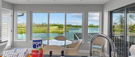 A kitchen with a view of a golf course and water body, a dining area with a table and chairs, and a large window.