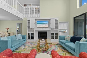Una sala de estar con televisor, sofás, chimenea y una escalera.
