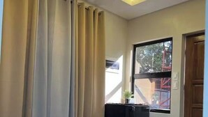 A room with a sofa, a small table, a window with curtains, and a door. - Cozy Stay at JAL Transient House (Hinoba-an)
