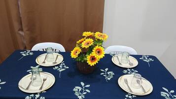 A table set for four with a vase of yellow flowers in the center, white plates, and clear glassware.