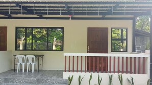 A covered outdoor area with a table and chairs, a wooden door, and windows overlooking greenery. - Cozy Stay at JAL Transient House (Hinoba-an)