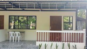 A covered outdoor area with a table and chairs, a wooden door, and windows overlooking greenery. - Cozy Stay at JAL Transient House (Hinoba-an)