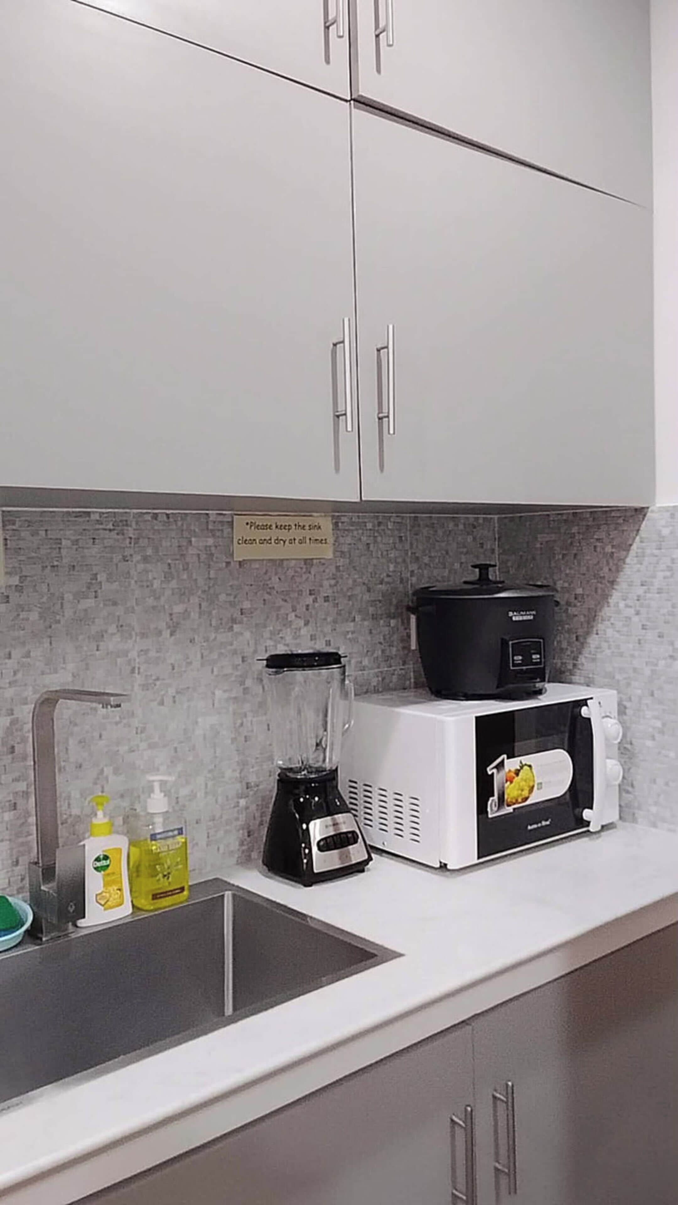 A kitchen with white cabinets, a sink, a blender, a microwave, and a slow cooker.