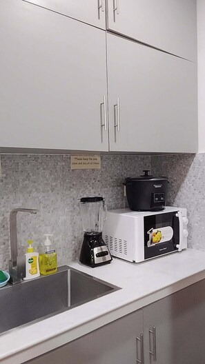 A kitchen with white cabinets, a sink, a blender, a microwave, and a slow cooker. - Cozy Stay at JAL Transient House (Hinoba-an)