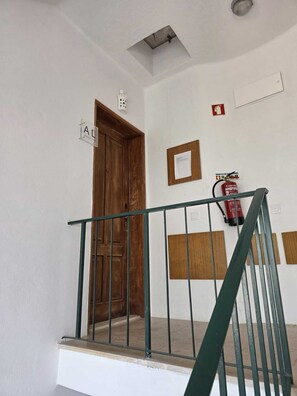 Eine Treppe mit Metallgeländer, einer Holztür und einem an der Wand befestigten Feuerlöscher.