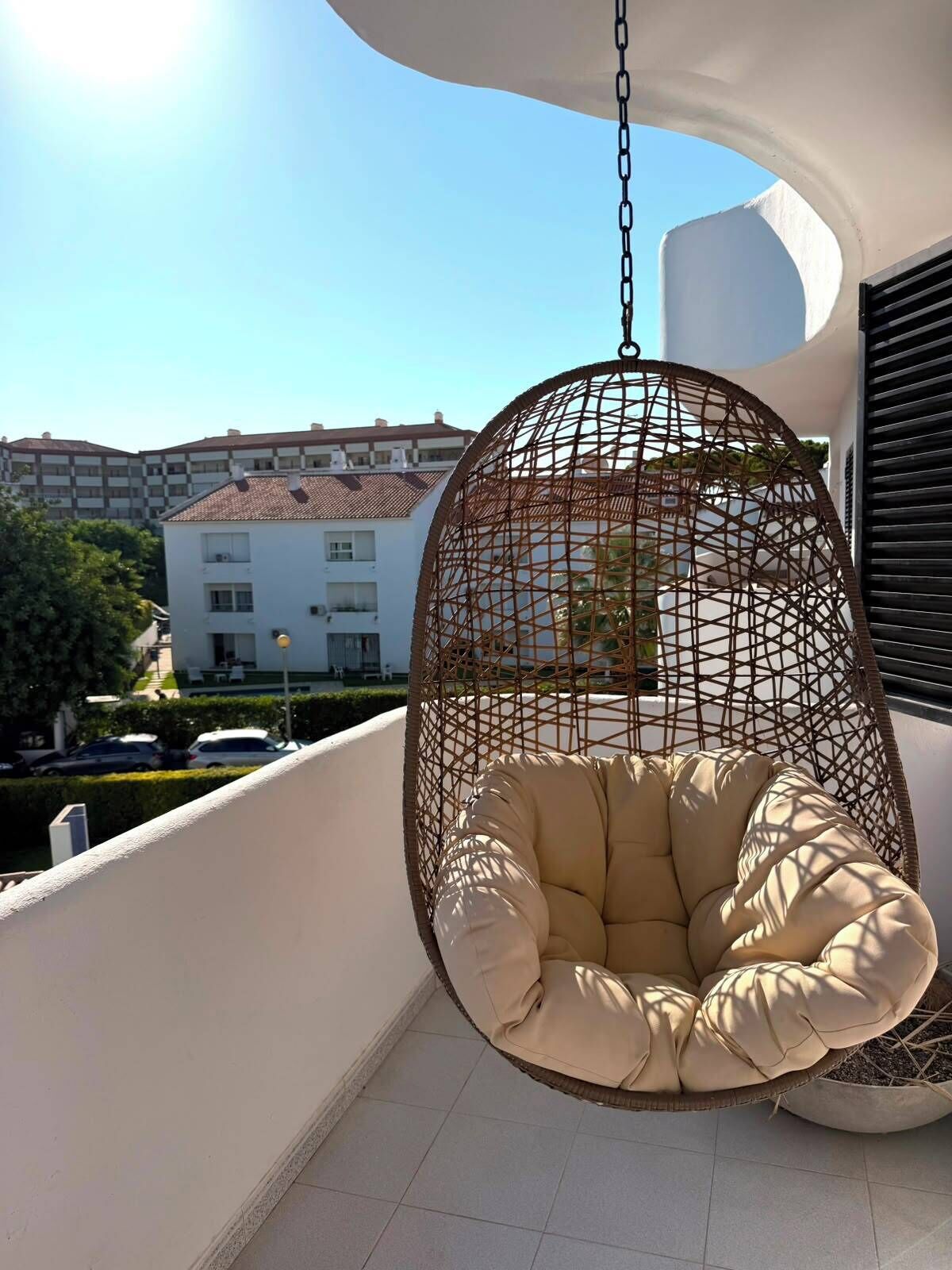 A hanging chair with a cushion on a balcony with a view of buildings in the background.