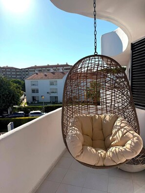 Ein Hängekorbstuhl mit Kissen auf einem Balkon mit Blick auf Gebäude im Hintergrund.