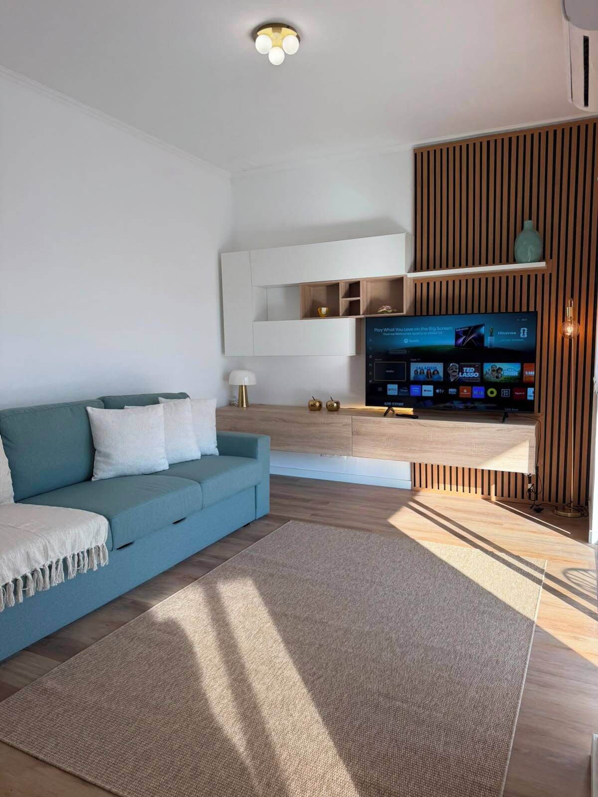 A modern living room with a sofa, a flat-screen TV, and a wooden accent wall.