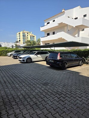 A parking area with several cars, a building with balconies, and a clear sky. - Solymar Vilamoura - Renovated Apartment with a Pool in a Quiet Area of Vilamoura (Quarteira)