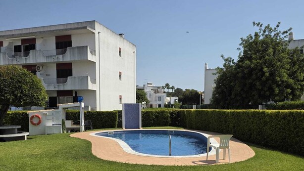 Una piscina rodeada de un césped cuidado, con un edificio al fondo.