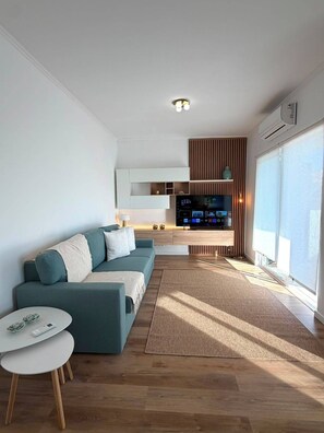 A modern living room with a sofa, a coffee table, and a TV in the background. - Solymar Vilamoura - Renovated Apartment with a Pool in a Quiet Area of Vilamoura (Quarteira)
