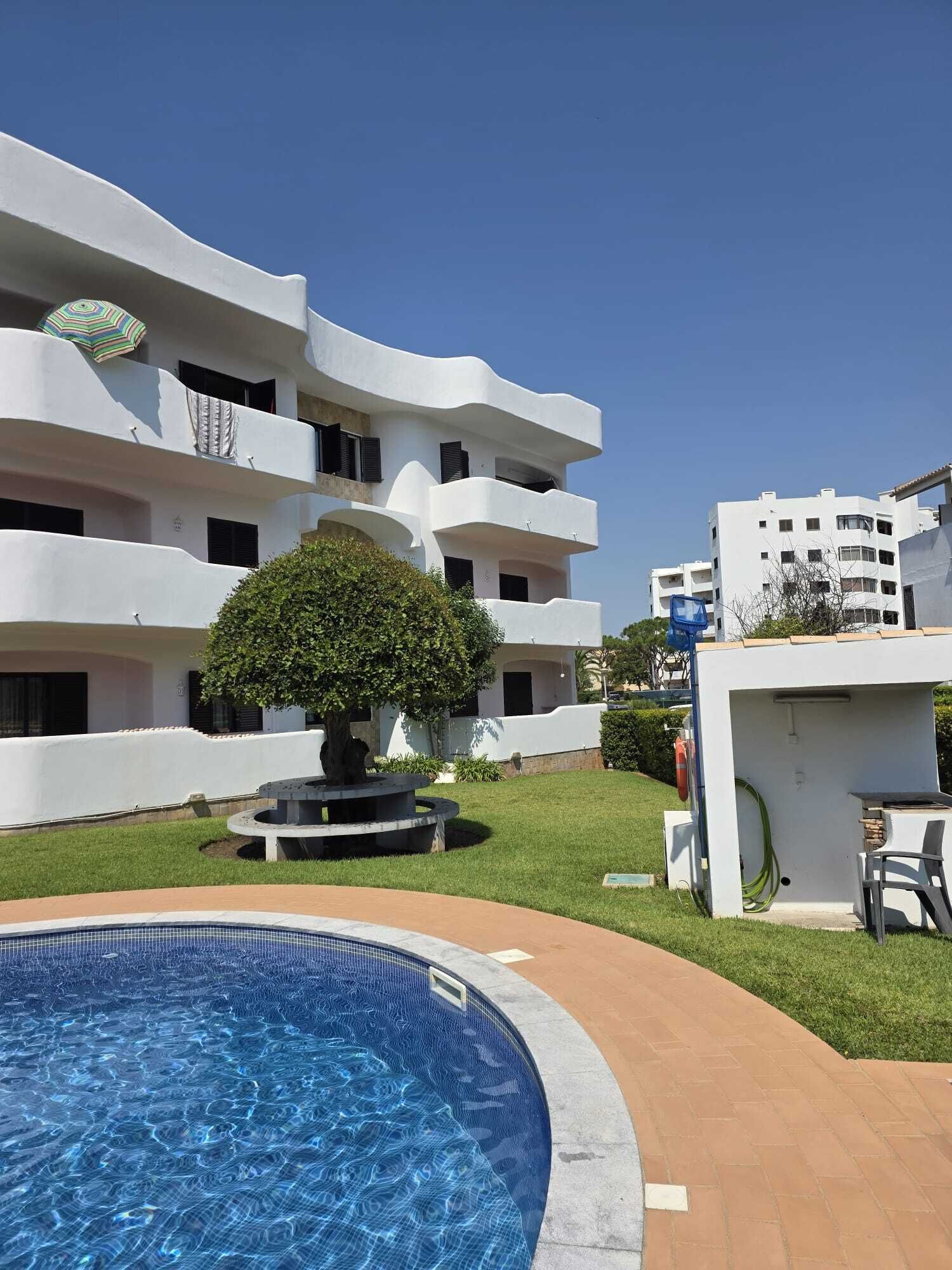 A swimming pool surrounded by a white building with multiple balconies and a small tree in the center.