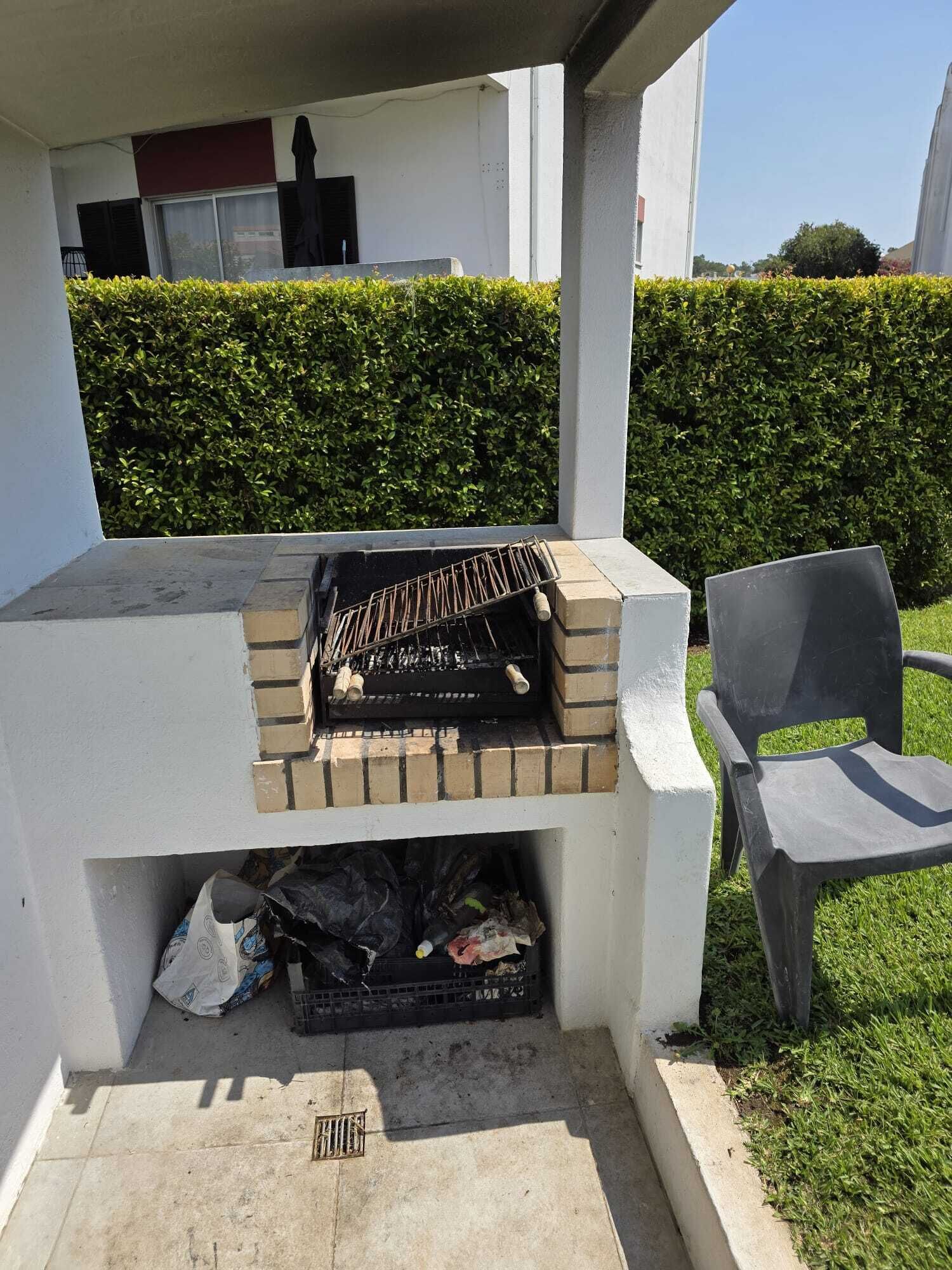 Un barbecue avec une base en briques, une grille en métal et une chaise à proximité.
