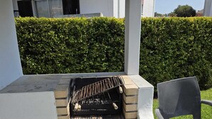 Una parrilla para barbacoa con base de ladrillo, una rejilla metálica y una silla cerca.