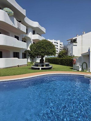A swimming pool with a fountain, surrounded by white buildings and a well-maintained lawn. - Solymar Vilamoura - Renovated Apartment with a Pool in a Quiet Area of Vilamoura (Quarteira)