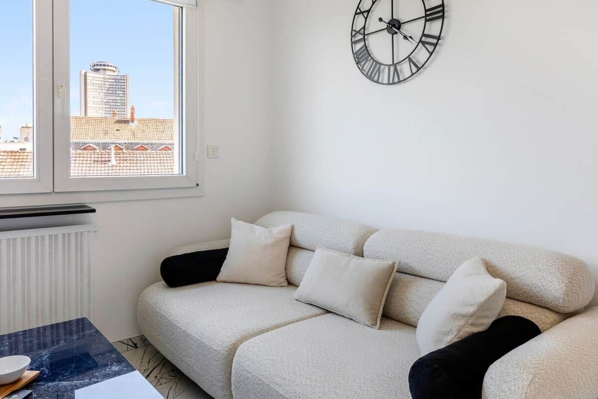 Un salón con sofá, un reloj, una ventana y un radiador.
