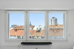Una habitación con un amplio ventanal que da a un paisaje urbano con edificios de techo rojo y un rascacielos moderno.
