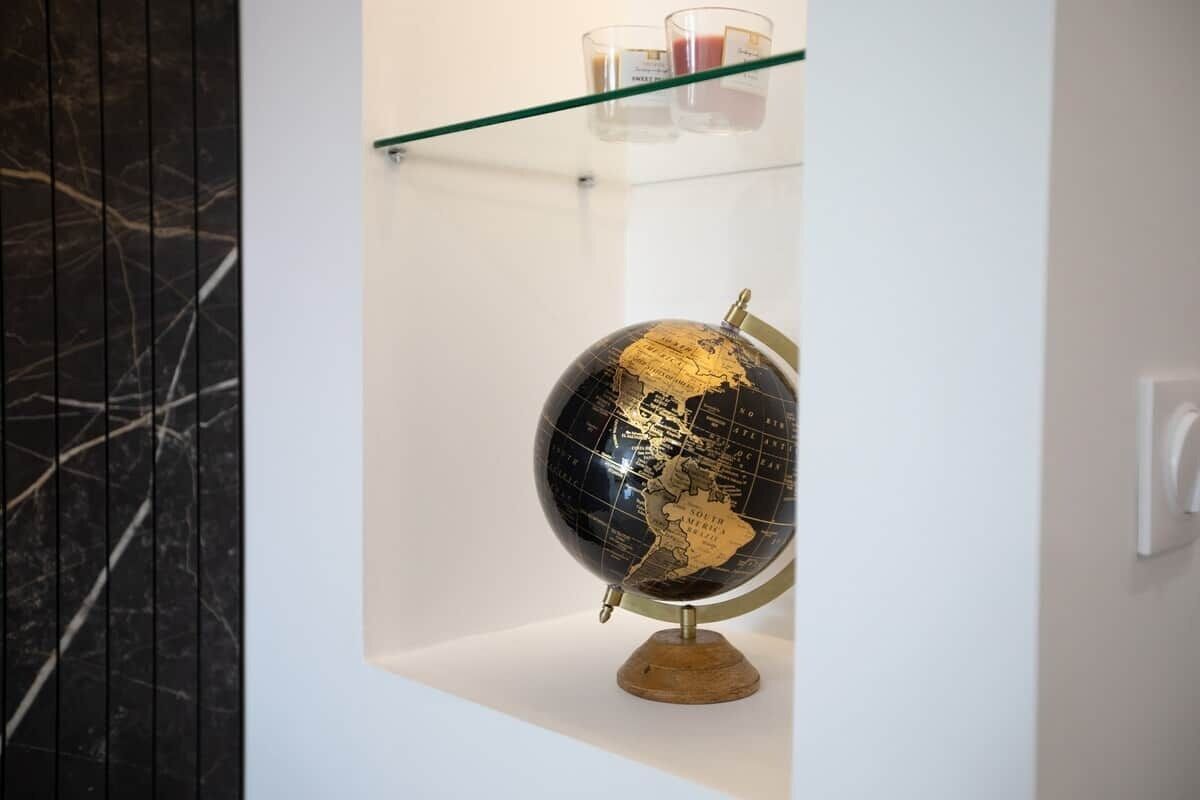 A globe on a wooden stand in a white display case with a glass shelf above it.
