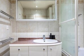 Un baño con un lavabo blanco, un espejo encima y una zona de ducha a la derecha.