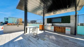 Um pátio externo com mesa, cadeiras, churrasqueira e televisão montada na parede.