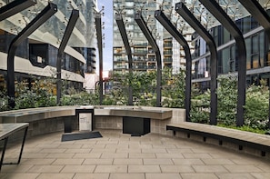 An outdoor seating area with a modern design, surrounded by greenery and overlooking a cityscape. - High-rise 2-bed Apt at Trio Boxhill With Car Park (Melbourne)