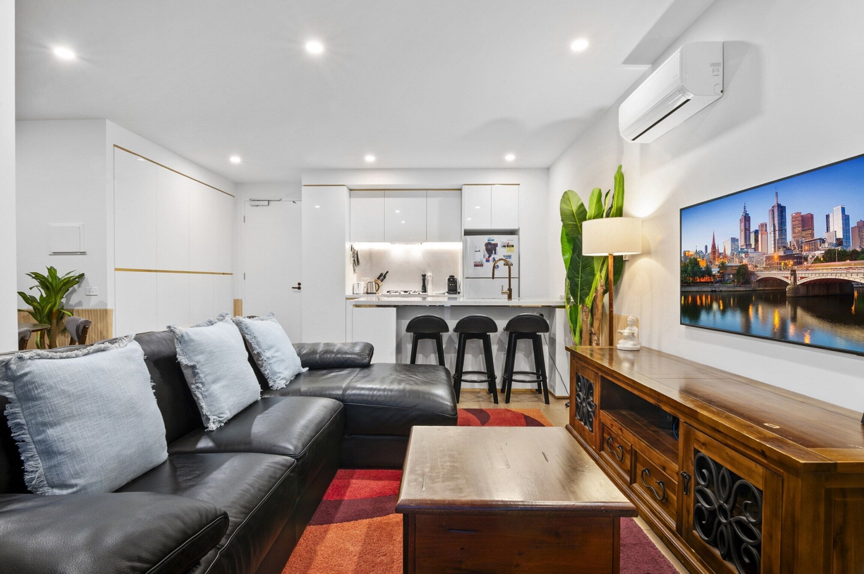 A modern living room with a black leather sofa, a wooden coffee table, and a cityscape TV.