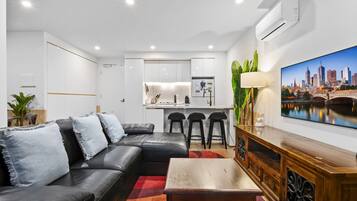 A modern living room with a black leather sofa, a wooden coffee table, and a cityscape TV.