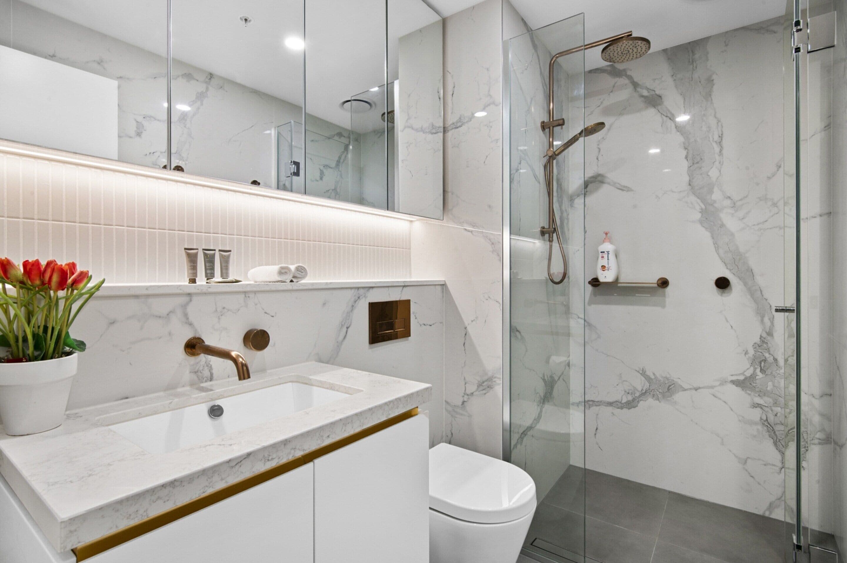 Un baño moderno con tocador de mármol, cabina de ducha de vidrio y retrete.