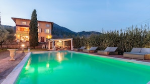 A swimming pool with lounge chairs, a covered seating area, and a building with multiple windows and lights. - Villa Near Lucca With Private Pool (Lucca)