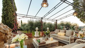 An outdoor patio with wicker furniture, a table with candles, and a hanging light fixture. - Villa Near Lucca With Private Pool (Lucca)