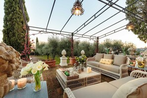 Eine Terrasse im Freien mit Korbmöbeln, einem Tisch mit Kerzen und einer hängenden Lampe.