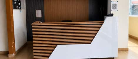 A reception desk with a slatted wooden design, a framed certificate on the wall, and a QR code on the right.
